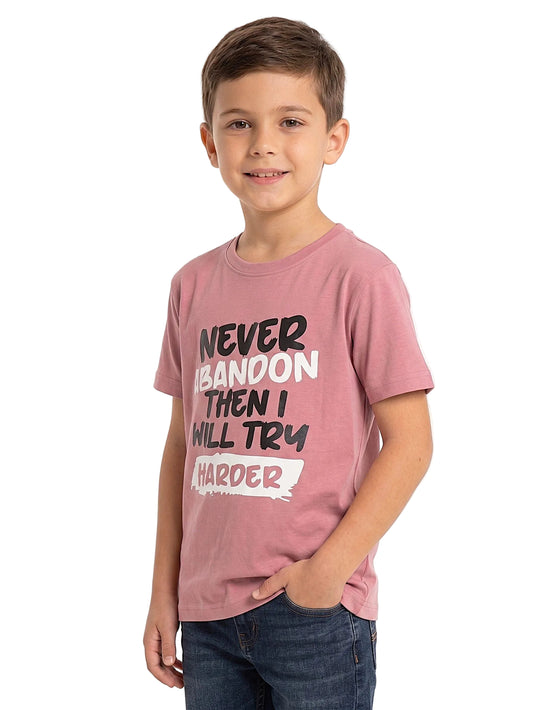 A young boy wearing a dusty rose pink graphic t-shirt with the motivational quote 'NEVER ABANDON THEN I WILL TRY HARDER' in black and white lettering, paired with dark blue jeans, photographed against a clean white background.