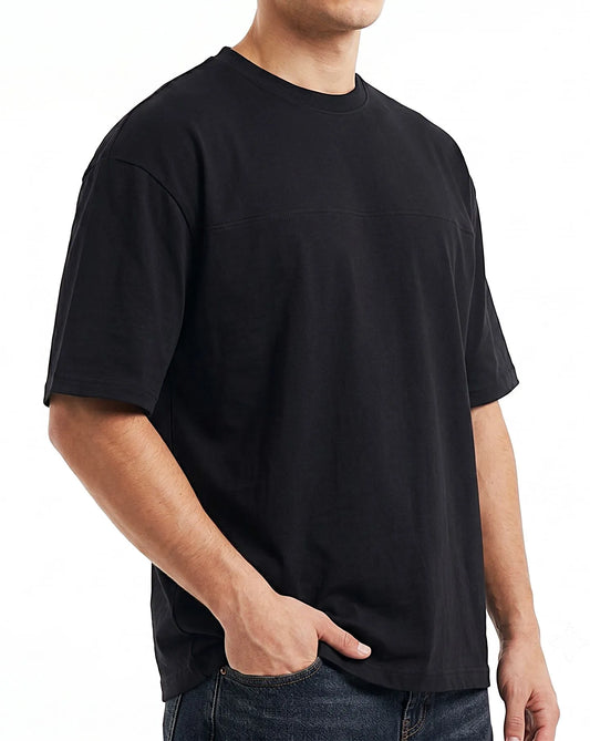 A man wearing a black short-sleeve crewneck t-shirt with a horizontal seam detail across the chest, paired with dark blue jeans, shown against a plain white background.