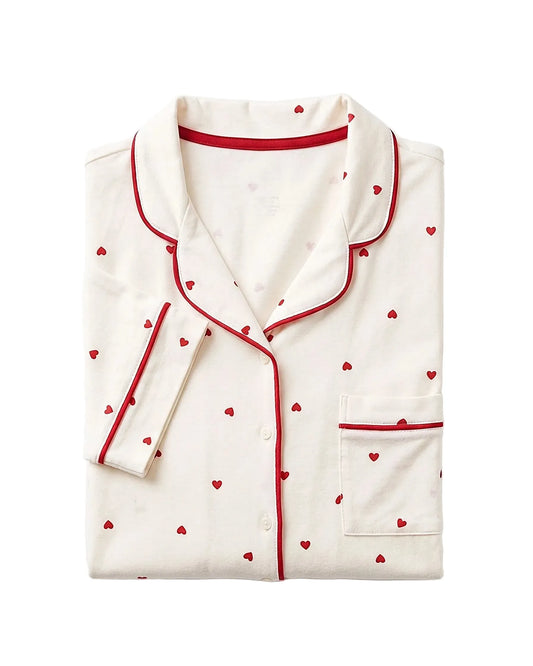 Neatly folded women's creamy white pajama shirt featuring an all-over red heart print, button-down front, and red contrast piping by TREE