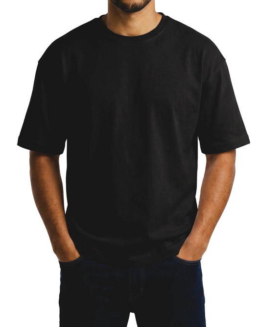 A man wearing a plain black short-sleeve crewneck t-shirt and dark jeans, standing against a light gray background.