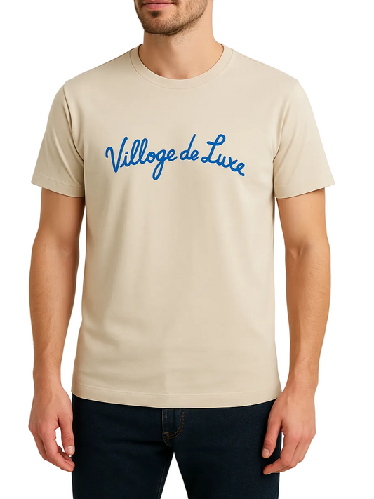 Beige t-shirt with blue 'Village de Luxe' text worn by a person on a plain background
