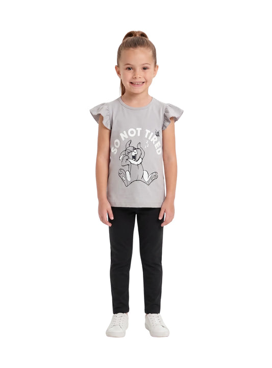 A young girl wearing a light grey t-shirt featuring a cartoon rabbit graphic and ruffle sleeves, paired with black pants and white sneakers