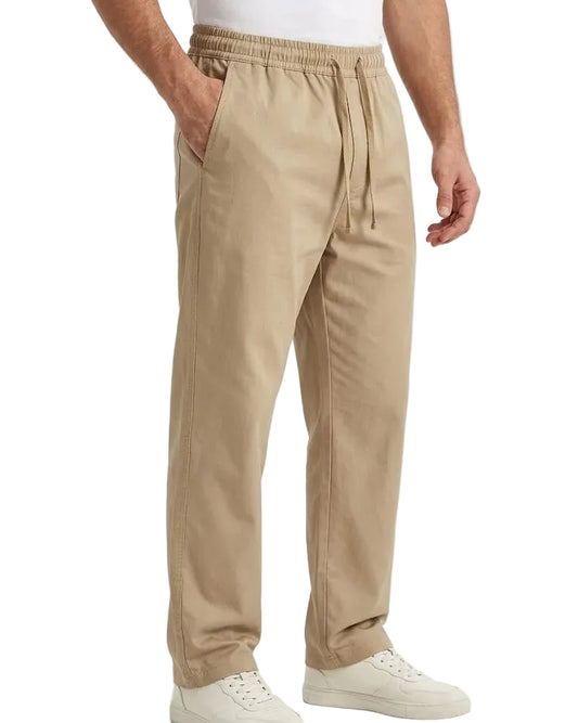 A person wearing beige drawstring jogger-style pants with side pockets, paired with white sneakers, shown from the waist down on a clean white studio background.