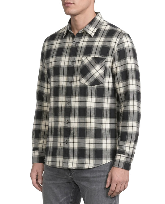 A man wearing a long-sleeve button-up plaid flannel shirt in black and cream, paired with gray jeans, shown from the chin down against a plain white background.