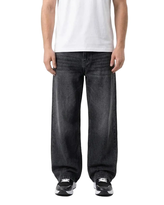 A person wearing very loose, wide-leg black denim jeans with a white t-shirt and black-and-white sneakers, shown from the chest down against a plain white studio background.