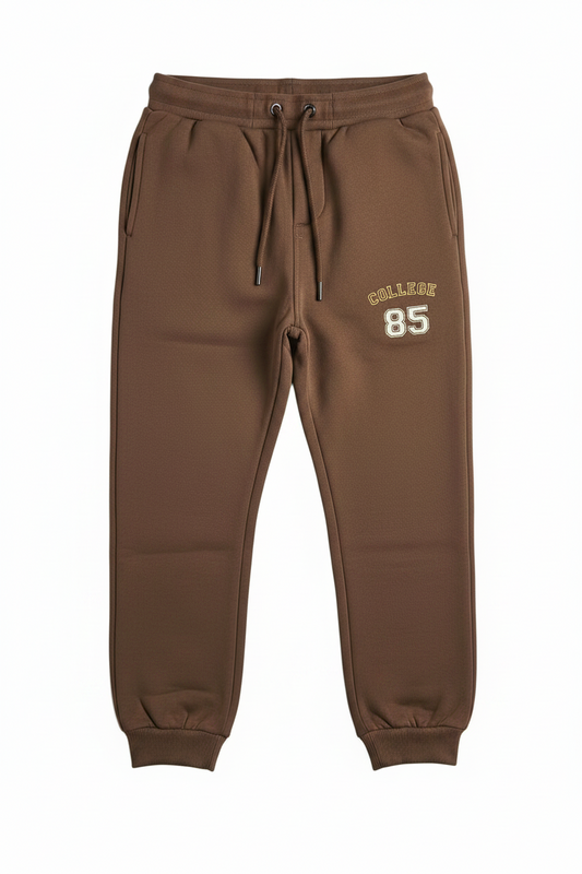 Brown sweatpants with a drawstring waist, side pockets, and 'COLLEGE 85' printed in gold on the left thigh, shown against a plain white background.