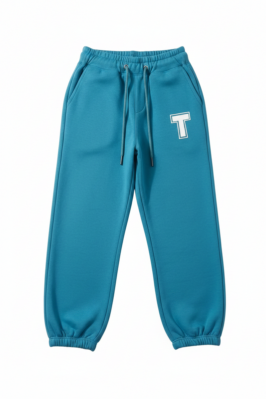 A pair of teal blue sweatpants with an elastic waistband, drawstring, and elastic cuffs. A white block letter 'T' with a black outline is printed on the left thigh.