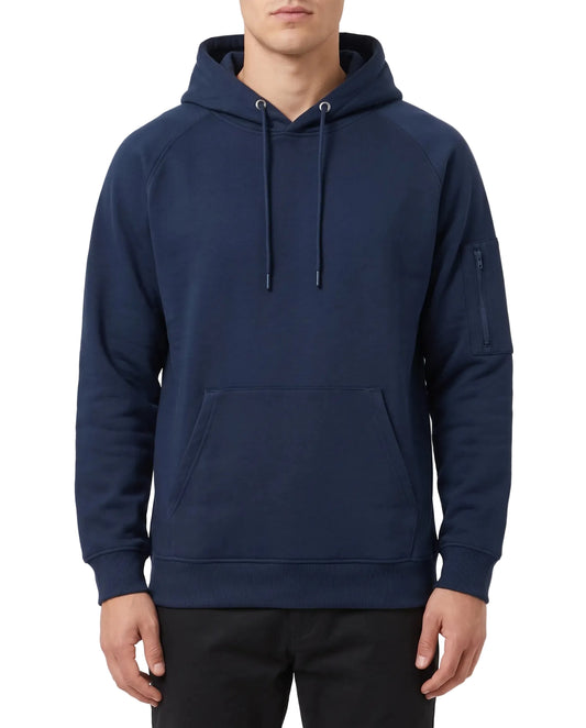 A man wearing a navy blue pullover hoodie with a kangaroo pocket and a zippered sleeve pocket, paired with black pants, against a plain light gray background.