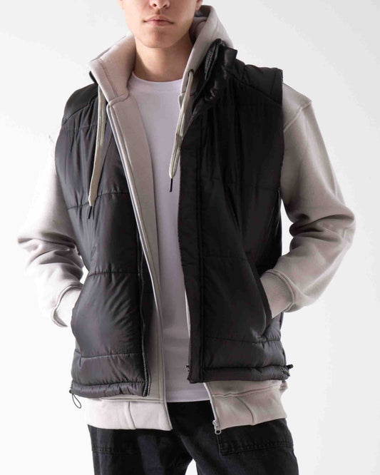 Person wearing a black puffer vest over a light gray hoodie on a white background