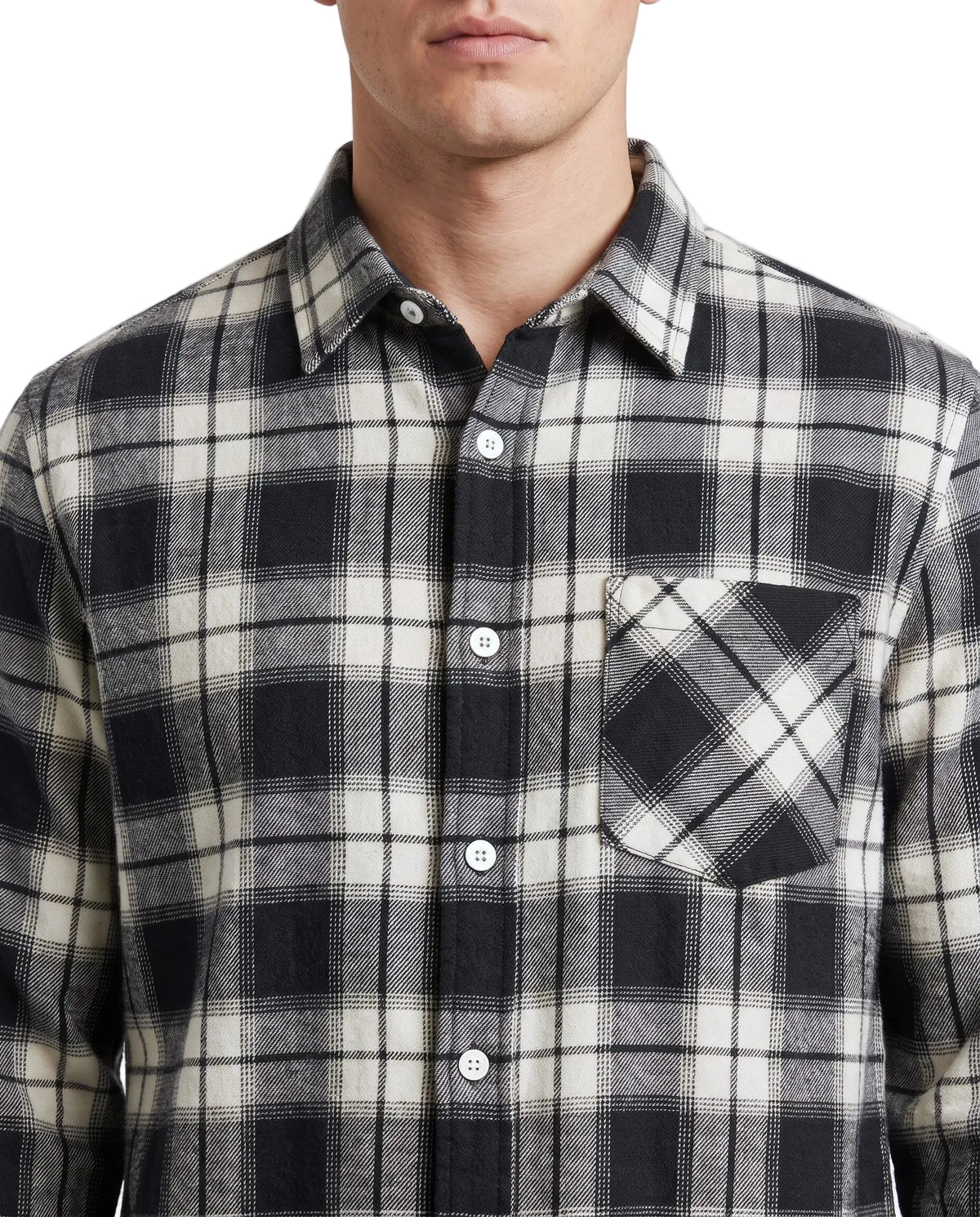 A close-up of a man wearing a black, gray, and off-white plaid button-down shirt with a chest pocket, set against a plain light background.