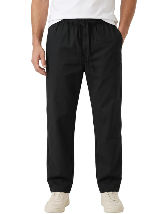 A person wearing black drawstring jogger-style pants with a white t-shirt and off-white sneakers, shown from the waist down against a plain white studio background.
