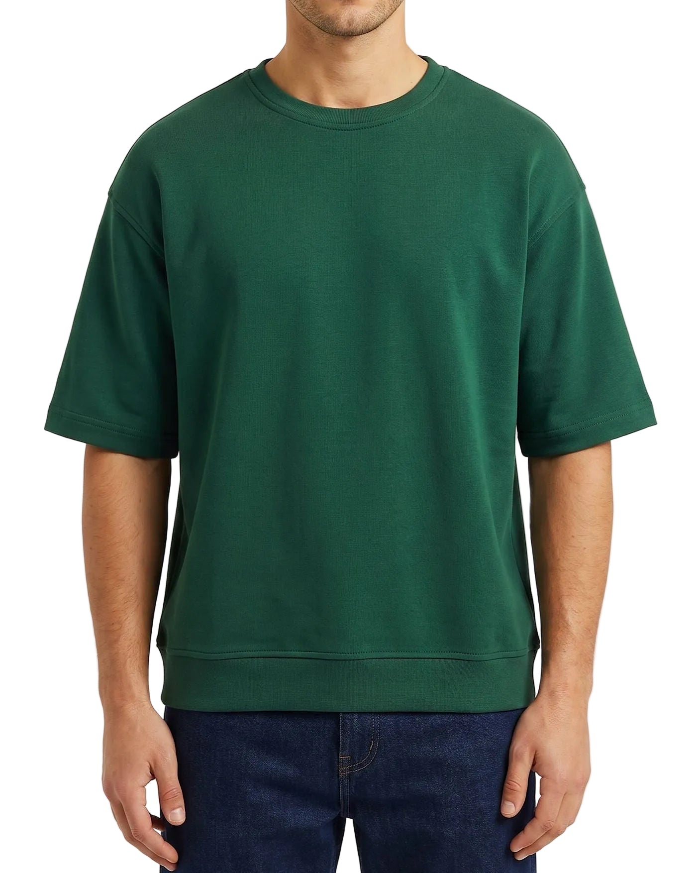 A man wearing an oversized dark green crewneck sweatshirt and dark blue jeans, shown from the neck down against a light off-white background.
