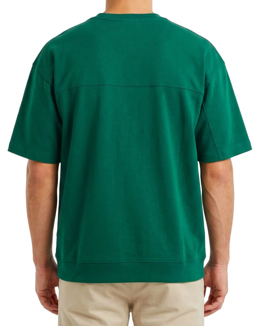 A man wearing a dark green short-sleeve crewneck t-shirt, viewed from the back, paired with beige pants against a plain white background.