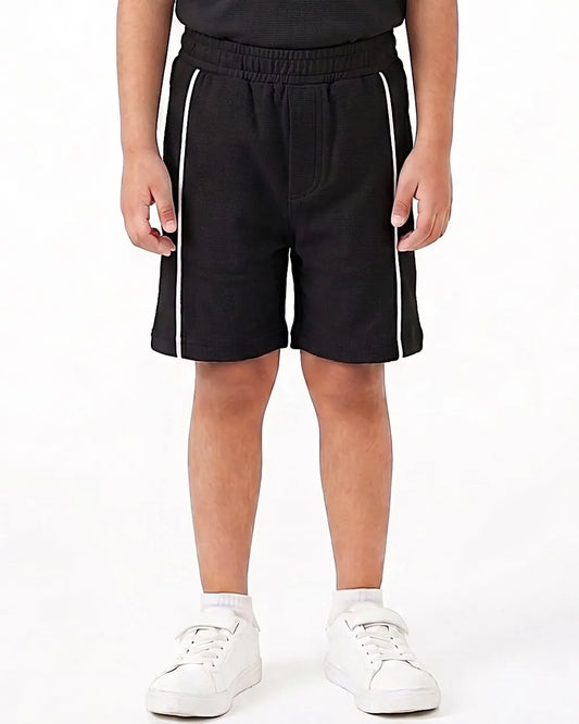 A child wearing black athletic shorts with white side stripes, paired with a black top and white sneakers, shown from the waist down on a white studio background.