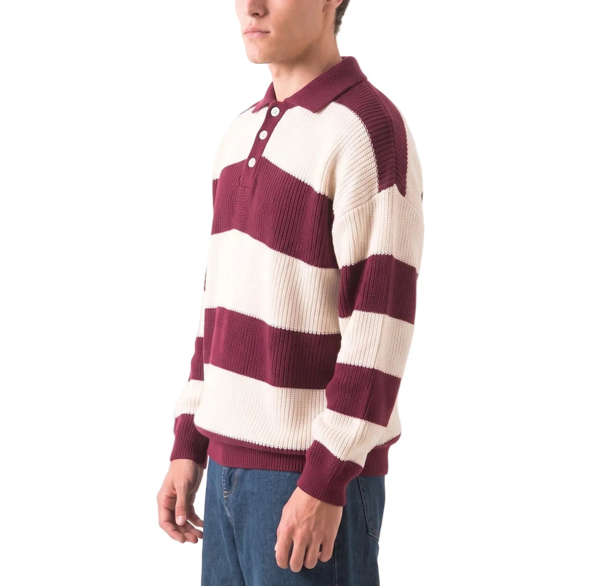 A man wearing a ribbed knit polo sweater with wide horizontal stripes in burgundy and cream, paired with blue jeans, shown against a plain white background.