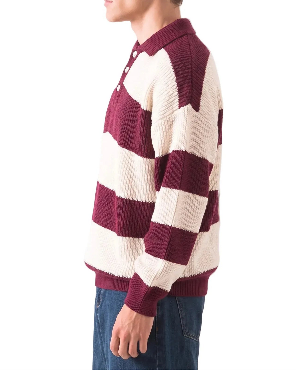 A man in profile wearing a maroon and cream striped knit polo sweater, paired with blue jeans, against a plain white background.
