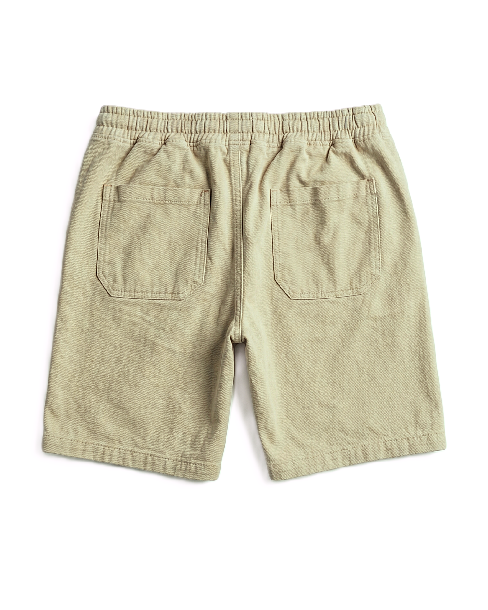 A pair of light khaki or beige shorts shown from the back, featuring an elastic waistband and two large patch pockets, laid flat on a white background.