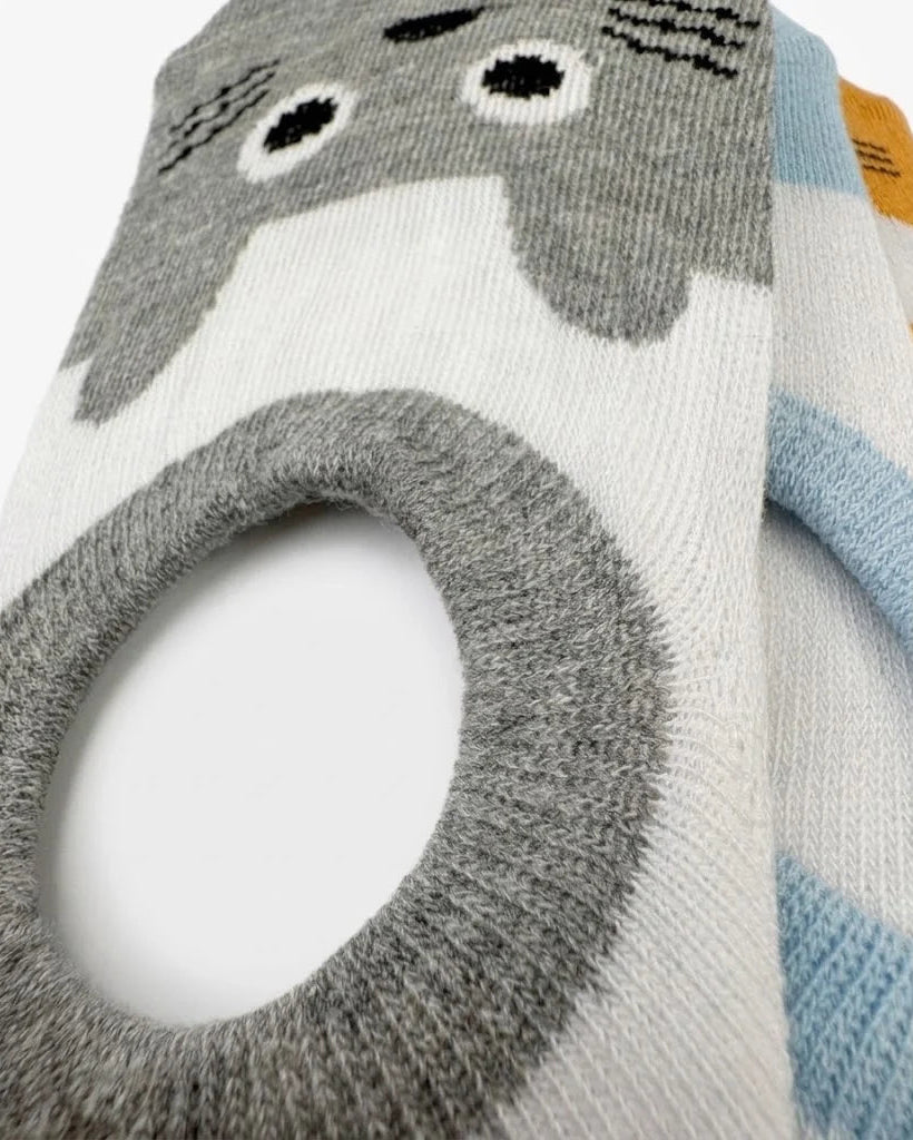 Close-up of a knit sock featuring a gray Totoro character face and body design on a white background, with a light blue striped section and a small orange tab visible.