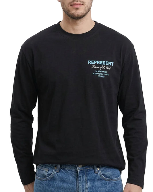 A man wearing a black long-sleeve crewneck t-shirt with a small white and light blue graphic print on the left chest, paired with blue jeans, against a plain white background.
