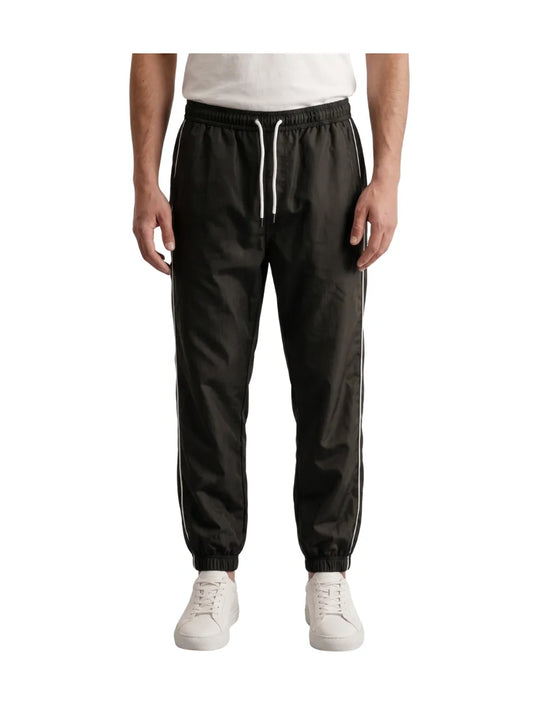 Front view of a man wearing dark grey athletic track pants with white side stripes by TREE
