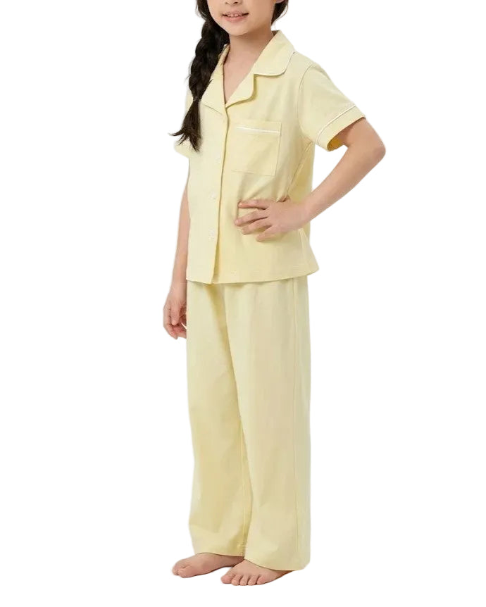 A young girl modeling a light yellow short-sleeve pajama set with matching wide-leg pants against a plain white studio background.