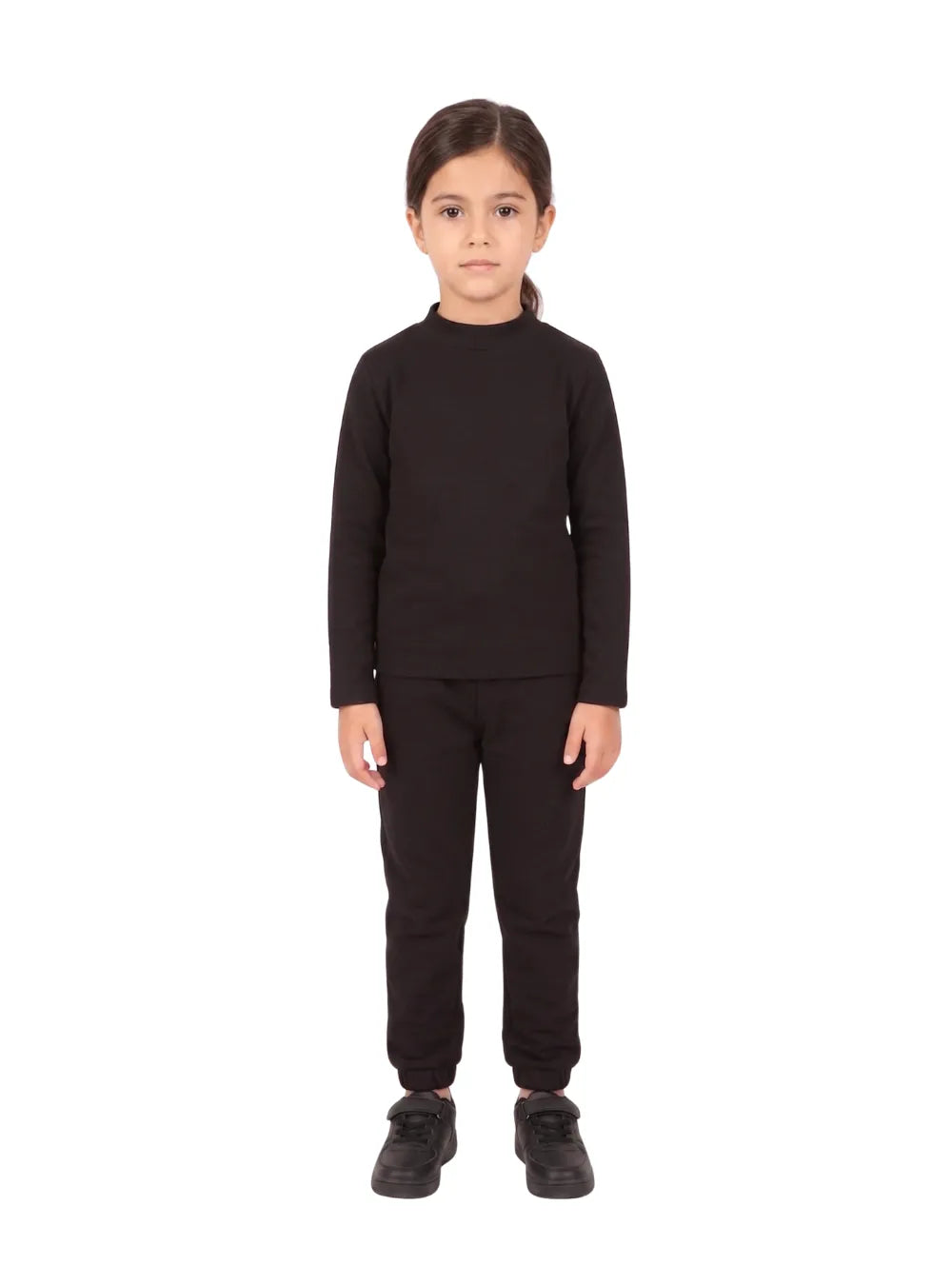 "Full-body front view of a young smiling girl wearing a Girls' Black High-Neck Basic Top with matching black pants and white sneakers against a white background