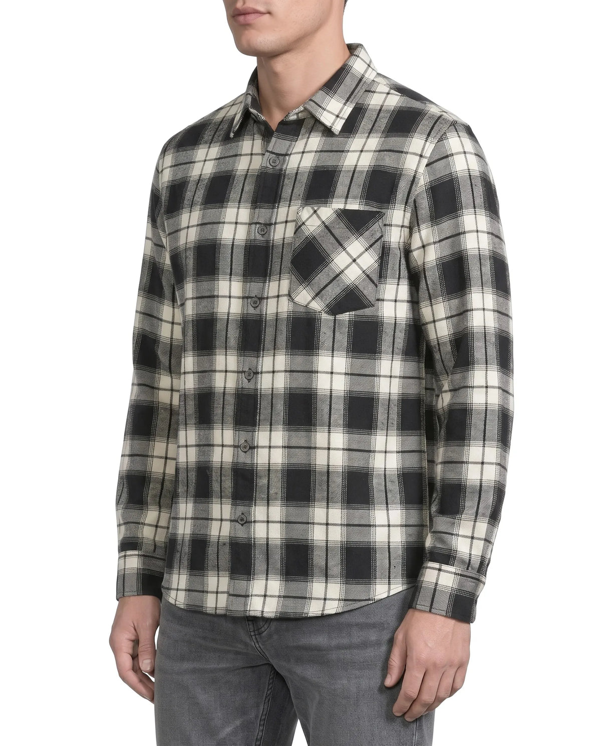 A man wearing a long-sleeve button-up plaid flannel shirt in black and cream, paired with gray jeans, shown from the chin down against a plain white background.