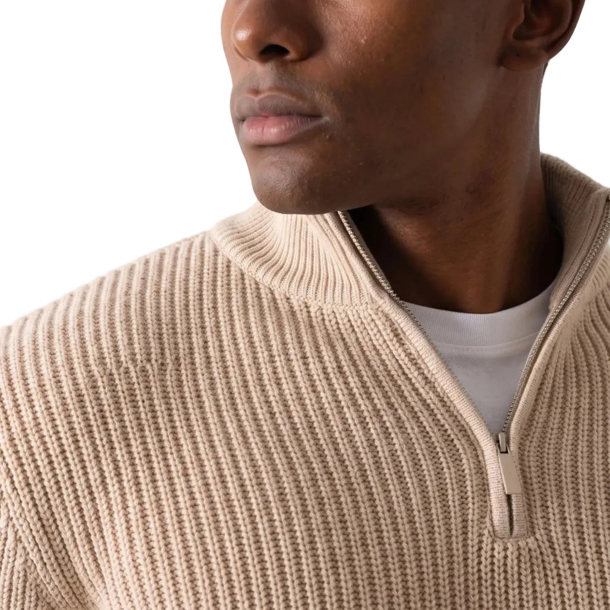 Close-up of a man wearing a beige ribbed knit quarter-zip sweater over a white t-shirt, against a plain light background.