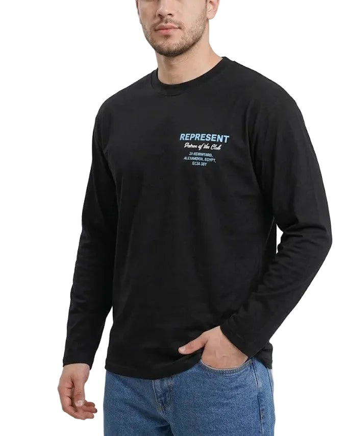 A man wearing a black long-sleeve t-shirt with a light blue graphic print on the left chest that reads 'REPRESENT Patron of the Club', paired with blue jeans, against a plain white background.
