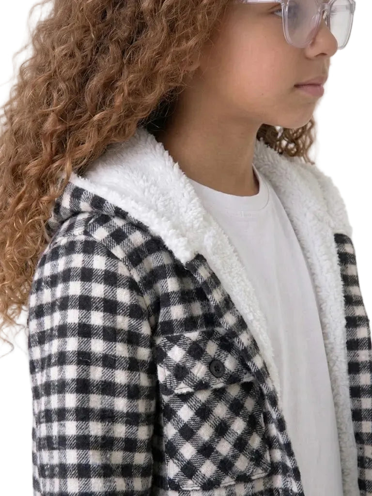 A close-up side profile of a child wearing a black and white checkered flannel jacket with a white lining, over a white t-shirt.