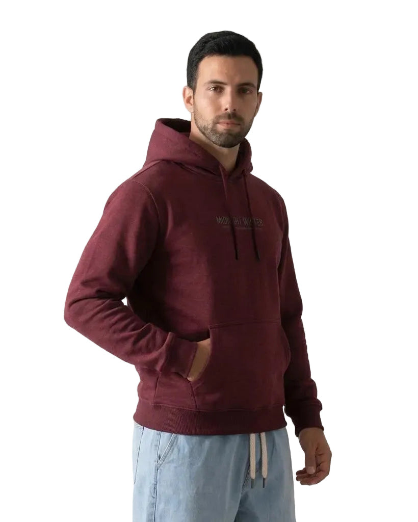 A man wearing a Burgundy hoodie with a kangaroo pocket and light blue sweatpants, standing against a plain white studio background.