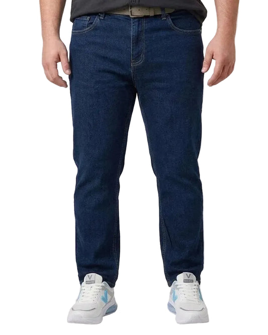 A person wearing dark blue big-size jeans, a dark gray shirt, and white sneakers, shown from the waist down against a light gray studio background.