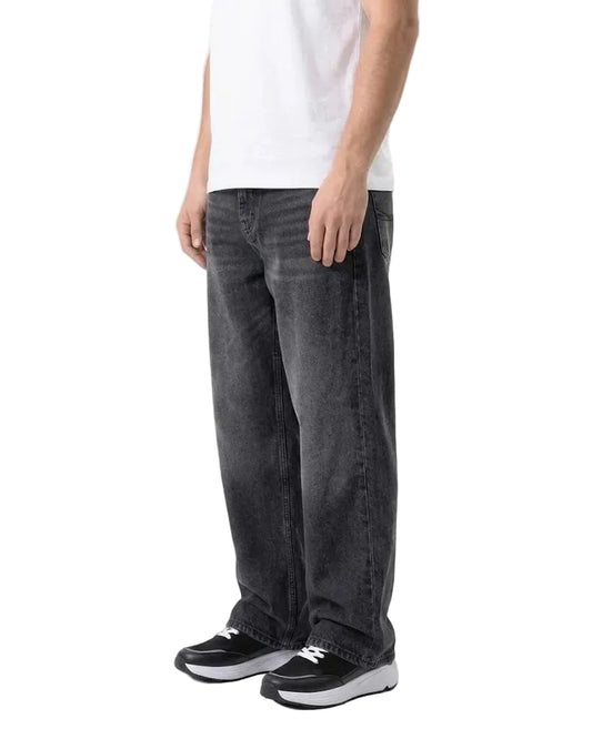 A person wearing loose-fit dark gray washed denim jeans with a white t-shirt and black sneakers, shown from the chest down against a plain white studio background.