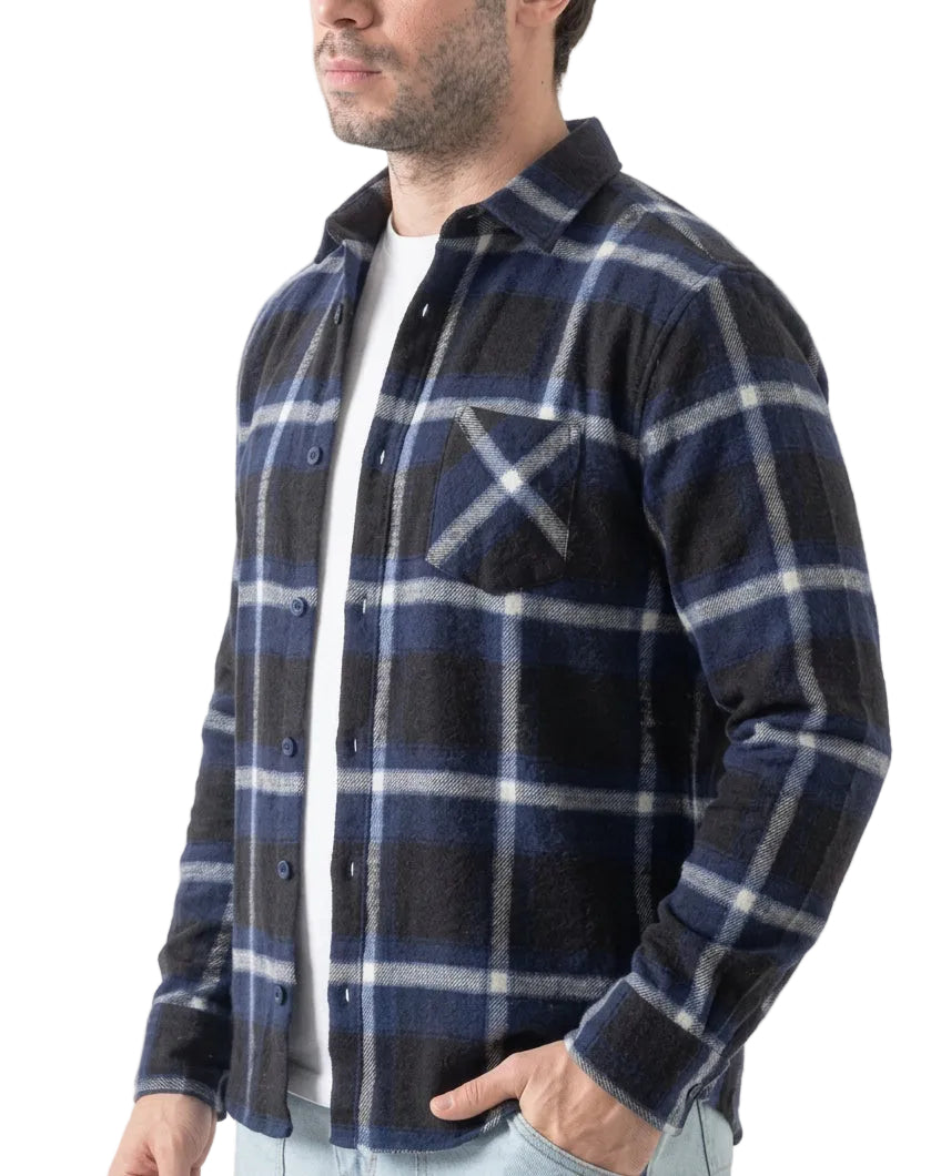A man wearing a navy blue and black plaid flannel shirt over a white t-shirt and light blue jeans, shown from the side against a white background.