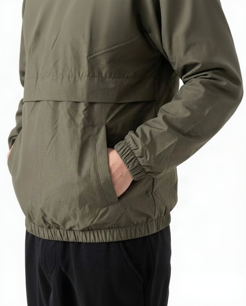 Close-up of a person wearing an olive green lightweight jacket, showing the side pocket with a hand inside and elasticized cuffs and hem, against a plain white background.