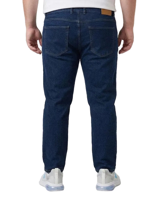 Rear view of a person wearing dark blue denim jeans with a white t-shirt and white sneakers, photographed against a light gray studio background.