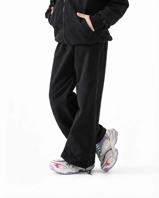 A person wearing black wide-leg sweatpants and a black zip-up hoodie, paired with gray and purple sneakers, shown from the waist down against a plain white background.
