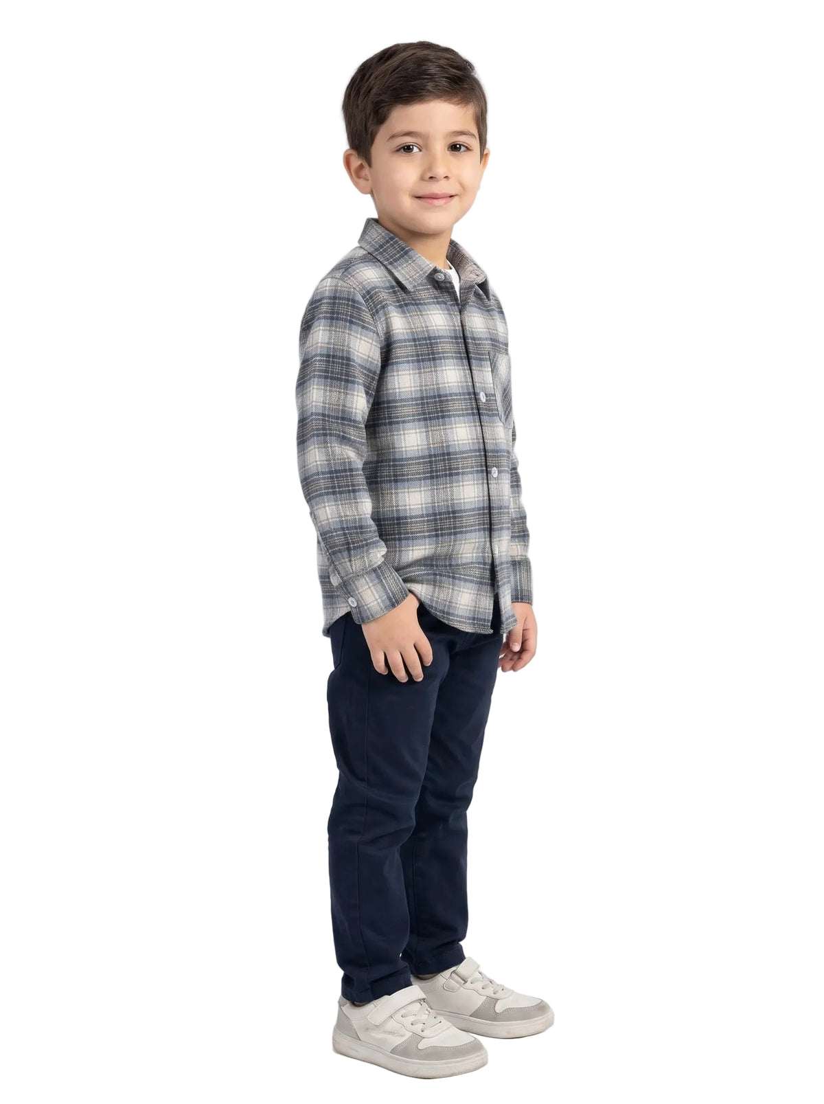 A young boy modeling a long-sleeve plaid button-up shirt in gray, white, and black, paired with dark navy pants and light gray sneakers, standing against a plain white studio background.