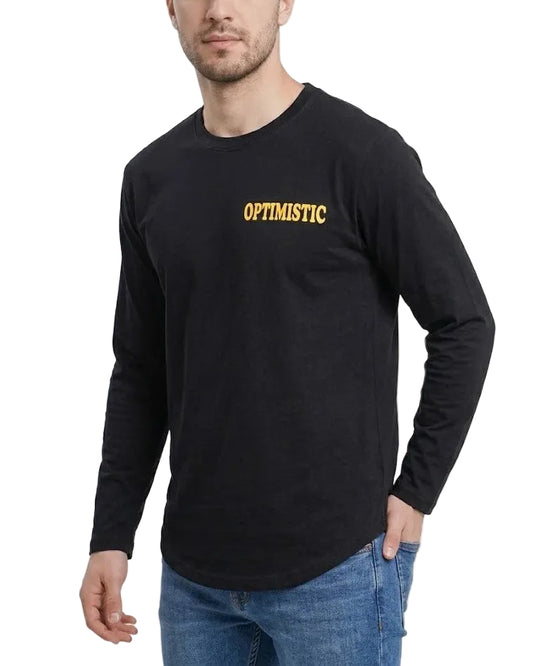 A man wearing a black long-sleeve t-shirt with 'OPTIMISTIC' printed in yellow text on the chest, paired with blue jeans, against a plain white background.