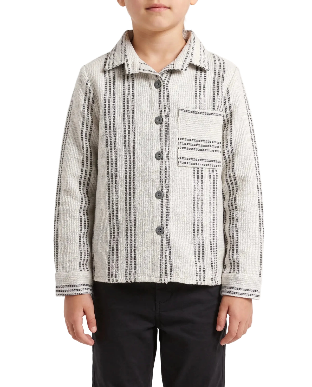 A child wearing a long-sleeve button-front shirt jacket with vertical black and gray dotted stripe patterns on a light beige fabric, paired with black pants, against a plain white studio background.