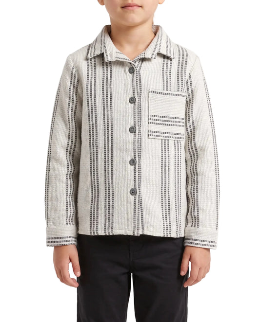 A child wearing a long-sleeve button-front shirt jacket with vertical black and gray dotted stripe patterns on a light beige fabric, paired with black pants, against a plain white studio background.