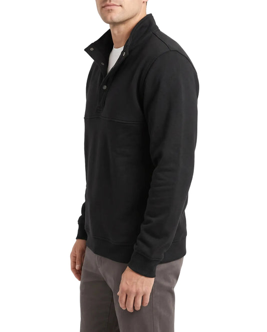 A man wearing a black long-sleeve quarter-zip pullover sweater with a stand collar, paired with gray pants, shown from a side profile against a plain white studio background.
