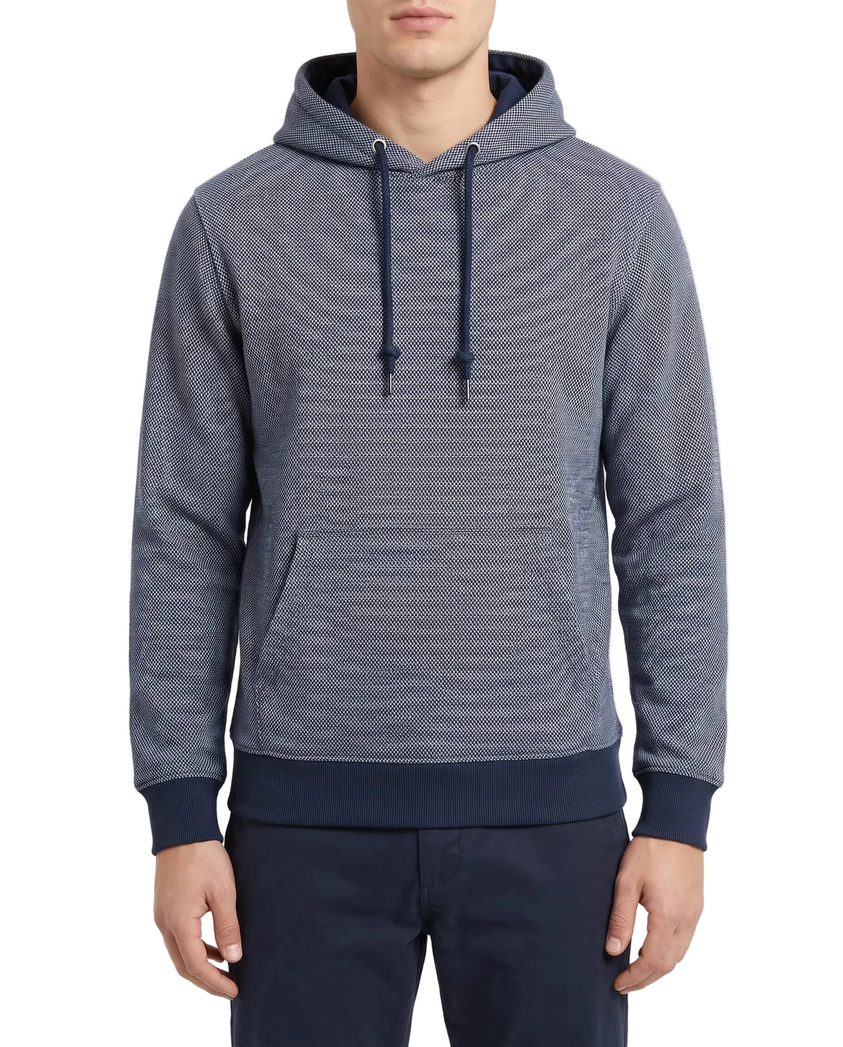 A man wearing a textured blue-gray pullover hoodie with dark navy ribbed cuffs, hem, and drawstrings, paired with navy pants, against a plain light background.