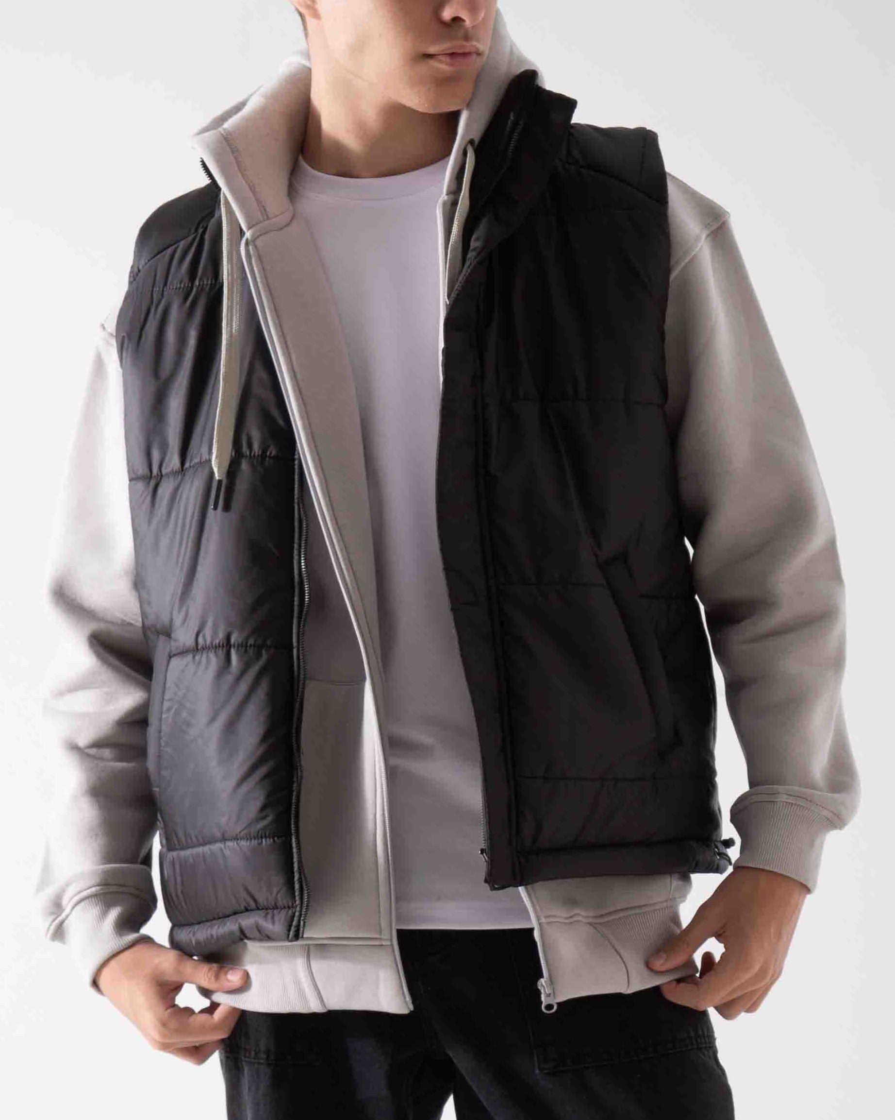 Person wearing a black puffer vest over a gray jacket on a white background